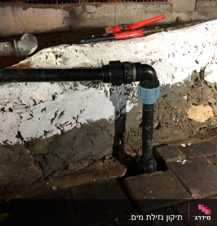צינור שחור עם מחבר פלסטיק כחול על קיר לבן